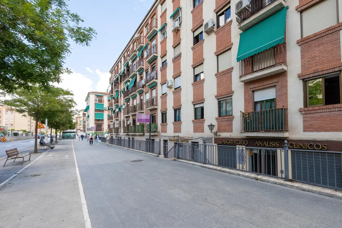 El edificio de la urbanización Alcázar del Genil donde están las viviendas, junto a un paseo arbolado